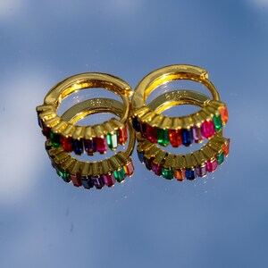 May include: A pair of gold hoop earrings with a rainbow of colorful rectangular stones. The earrings are made of metal and have a polished finish.