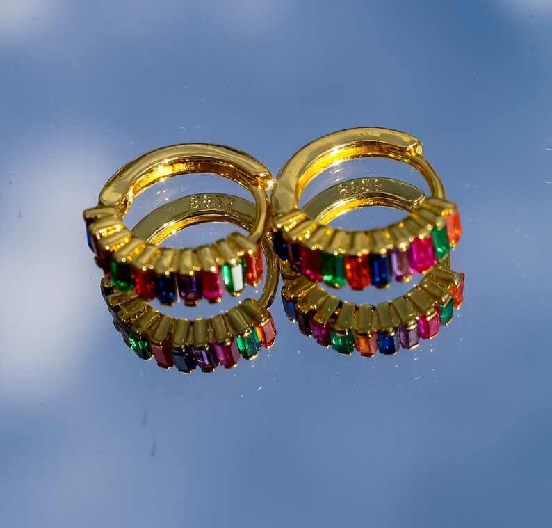 May include: A pair of gold hoop earrings with a rainbow of colorful rectangular stones. The earrings are made of metal and have a polished finish.
