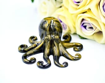 Puede incluir: Una figurita de pulpo de cerámica negra y dorada con ocho tentáculos. El pulpo está sentado sobre una superficie blanca.