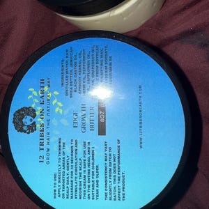 Puede incluir: Dos envases negros de manteca para el crecimiento del cabello con etiquetas azules. Las etiquetas enumeran los ingredientes e instrucciones de uso. El texto de la etiqueta dice "12 Tribes on Earth" y "Edge Growth Butter". Cada envase contiene 227g.