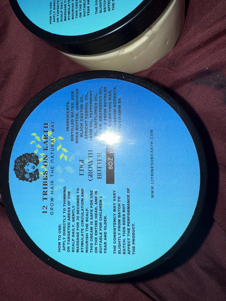 Puede incluir: Dos envases negros de manteca para el crecimiento del cabello con etiquetas azules. Las etiquetas enumeran los ingredientes e instrucciones de uso. El texto de la etiqueta dice "12 Tribes on Earth" y "Edge Growth Butter". Cada envase contiene 227g.