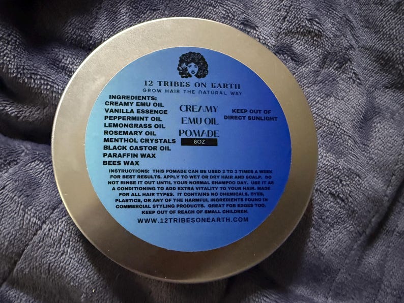 May include: A round metal tin of 12 Tribes on Earth Creamy Emu Oil Pomade. The blue label features the brand name, ingredients list including emu oil, vanilla, peppermint, lemongrass, rosemary, menthol, castor oil, paraffin, and beeswax, plus 8oz net weight.
