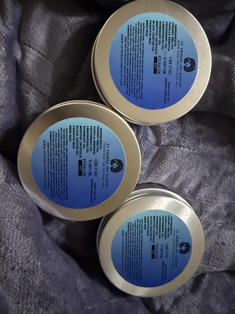 May include: Three round gold-colored metal tins of 12 Tribes on Earth Creamy Emu Oil Pomade. Each lid features a blue circular label with black text listing ingredients including emu oil, vanilla essence, peppermint oil, and beeswax, plus 8oz weight.