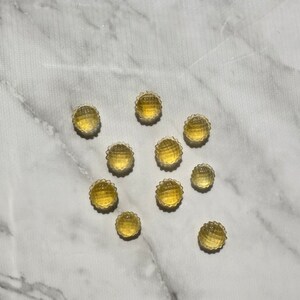 May include: A group of 10 small, round, yellow, translucent candies with a textured surface. The candies are arranged in a star shape on a white marble surface.
