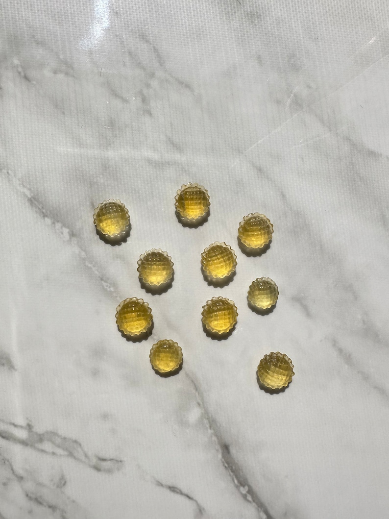 May include: A group of 10 small, round, yellow, translucent candies with a textured surface. The candies are arranged in a star shape on a white marble surface.