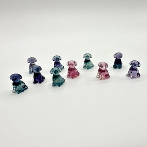 May include: A collection of ten small glass figurines of dogs in various shades of blue, purple, and pink.
