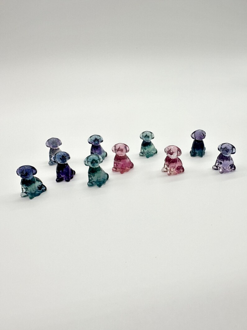May include: A collection of ten small glass figurines of dogs in various shades of blue, purple, and pink.