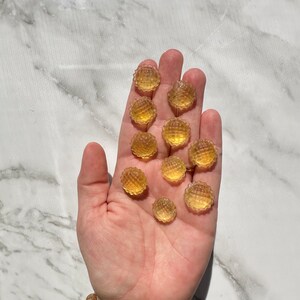 May include: A hand holding a group of small, round, yellow gummy candies. The candies have a textured surface and are arranged in a loose pile.