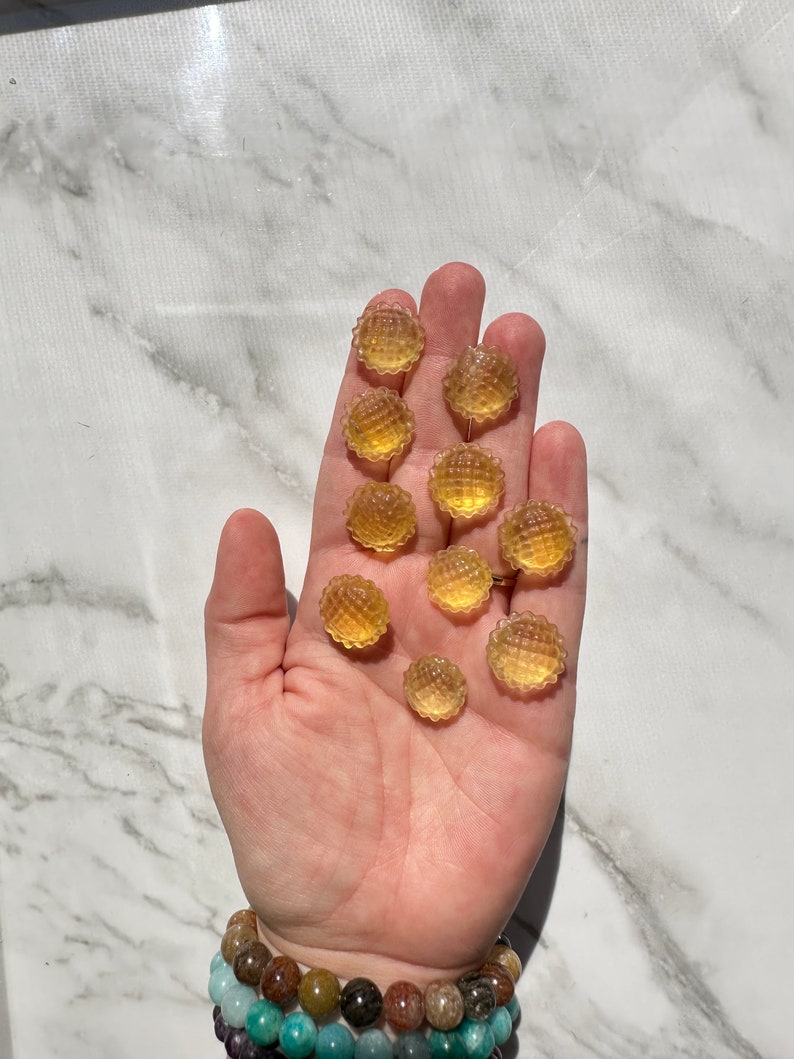May include: A hand holding a group of small, round, yellow gummy candies. The candies have a textured surface and are arranged in a loose pile.