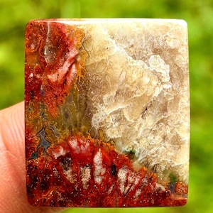 Könnte beinhalten: Ein quadratischer Edelstein mit einem natürlichen Muster. Der Stein weist eine Mischung aus Farben auf, darunter tiefe Rottöne, Orange und cremiges Beige. Die komplizierten Muster ähneln einer Landschaft oder einem abstrakten Design mit polierter Oberfläche.