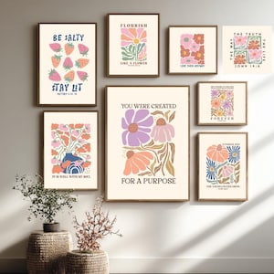 Puede incluir: Una colección de láminas artísticas enmarcadas con diseños florales e inspiradores. Las láminas presentan varias paletas de colores, incluyendo rosa, naranja y azul, con textos como "Be Salty" y "You Were Created". La obra de arte se exhibe en una pared neutra.
