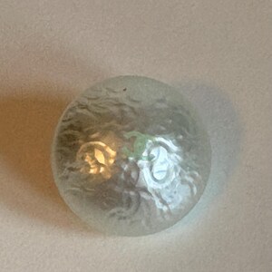 May include: A clear, frosted glass sphere with an internal design. The sphere has a textured surface and appears to have a light source within, creating a soft glow. The design inside is visible, adding visual interest.