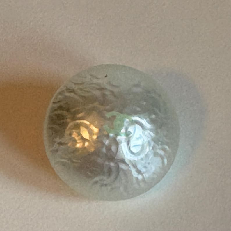 May include: A clear, frosted glass sphere with an internal design. The sphere has a textured surface and appears to have a light source within, creating a soft glow. The design inside is visible, adding visual interest.