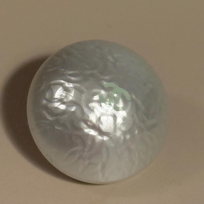 May include: A pearlescent, oval-shaped object with a swirling, textured surface. The object has a subtle sheen and a light green marking. The overall appearance is smooth and reflective, suggesting a decorative item.
