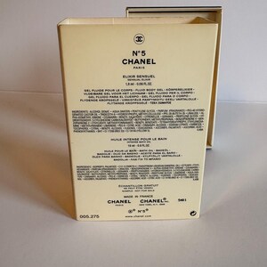 May include: A beige box of Chanel N&deg;5 Elixir Sensuel, 1.8 ml, and Intense Bath Oil, 19 ml. The box features the Chanel logo and product information in multiple languages. The text "Sample - Not for Sale" is also visible.