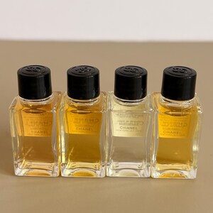 May include: Four small, rectangular perfume bottles with black caps. The bottles are filled with a golden-colored liquid. The bottles have the brand name "CHANEL" printed on them.