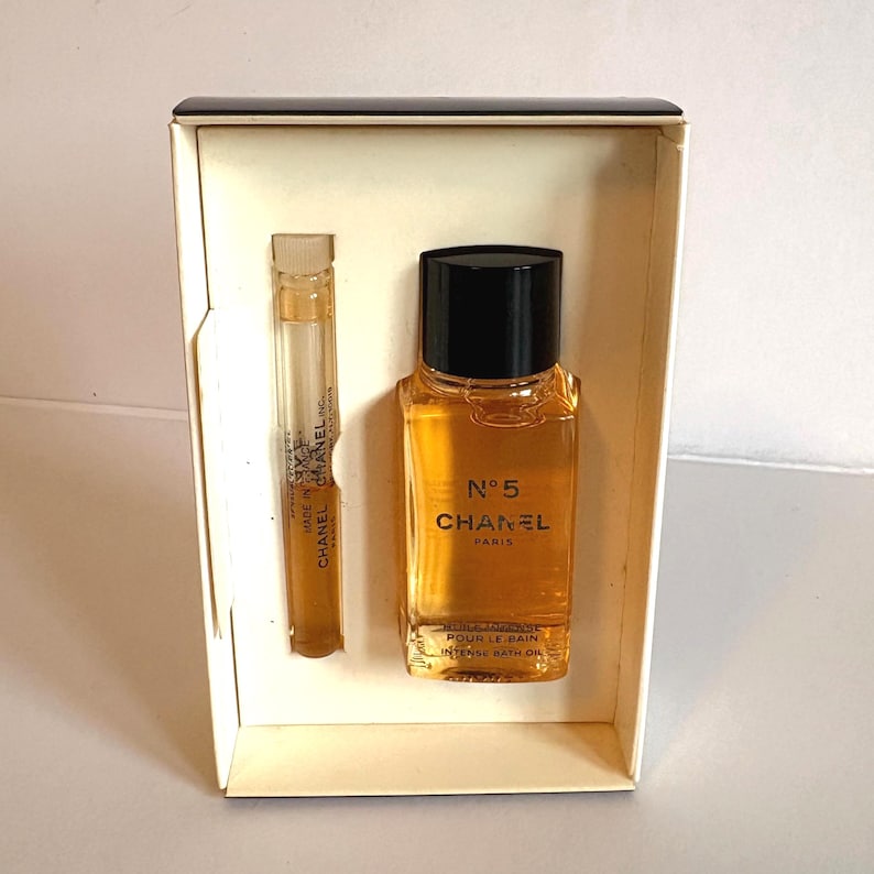 May include: A boxed set featuring a small bottle of Chanel No. 5 Intense Bath Oil and a sample vial. The bath oil bottle is rectangular with a black cap, and the label reads "N&deg;5 CHANEL PARIS". The sample vial is clear.