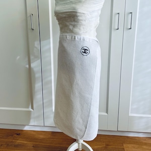 May include: White waffle-weave wrap skirt with a black and white logo patch. The skirt is wrapped around a form, showcasing its design and texture. The logo is circular and features interlocking C's.