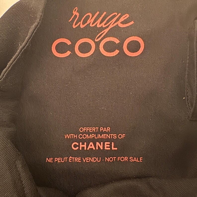 May include: Black fabric with the words "rouge COCO" in red script. Below, the text reads "OFFERT PAR WITH COMPLIMENTS OF CHANEL NE PEUT &Ecirc;TRE VENDU - NOT FOR SALE" in red. The fabric has a subtle texture.