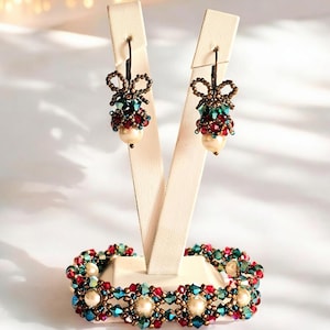 Puede incluir: Un conjunto de pendientes y una pulsera de cuentas con un esquema de color rojo, verde y dorado. Los pendientes tienen forma de campana con un lazo en la parte superior. La pulsera es una banda ancha con un patrón repetido de cuentas.