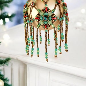 Könnte beinhalten: Ein goldener Weihnachtsbaumschmuck mit einem Perlenmuster in Grün-, Rot- und Goldtönen. Der Schmuck hat einen Fransen aus Perlen, der von unten hängt.