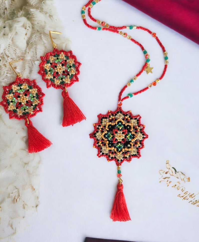 May include: A red beaded necklace and earrings set with a mandala design. The necklace and earrings feature red, green, black, and gold beads. The necklace has a gold star charm and a red tassel. The earrings have red tassels.