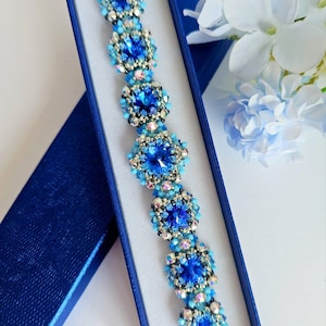 May include: A blue and turquoise beaded bracelet with a silver clasp, displayed in a blue box.