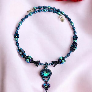 May include: A beaded necklace with a teardrop pendant. The necklace is made of iridescent blue and black beads, and the pendant is a teardrop-shaped crystal with a green and blue iridescent finish.