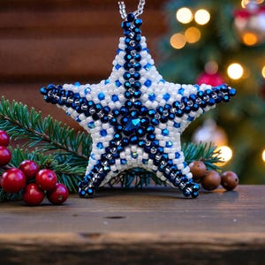 May include: A beaded star ornament with white and blue beads. The star has a five-point design with a central blue gem. The ornament is hanging in front of a Christmas tree with red berries and pine needles.