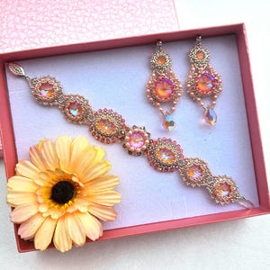 May include: A pink and gold beaded bracelet and earrings set. The bracelet is made with iridescent pink beads and gold accents. The earrings are dangle earrings with a similar design.