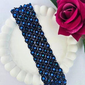 Könnte beinhalten: Ein gewebtes Armband aus schwarzen und blauen Perlen. Das Armband besteht aus kleinen, runden blauen Perlen und schwarzem Garn.