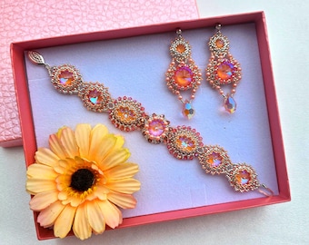 May include: A pink and gold beaded bracelet and earrings set in a pink gift box. The jewelry features iridescent pink and gold beads in a floral design.