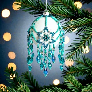 Könnte beinhalten: Ein weißer Weihnachtsschmuck mit aufwendiger türkis- und blaufarbener Perlenarbeit. Der Schmuck hat ein Schneeflocken-Design und baumelnde Perlenakzente. Er hängt an einer silbernen Kappe und einem weißen Faden, ideal für die Weihnachtsdekoration.