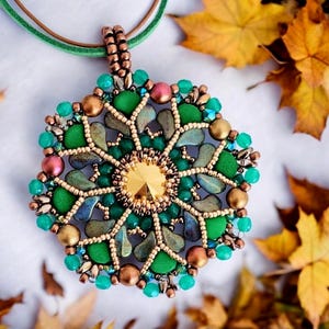 May include: A circular pendant featuring a central gold crystal surrounded by intricate beadwork in shades of green, bronze, and copper. The design incorporates small metallic and matte beads arranged in a radial pattern, suspended from a green cord.