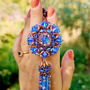 May include: A blue and copper beaded pendant with a tassel. The pendant is in the shape of a flower with a central crystal.