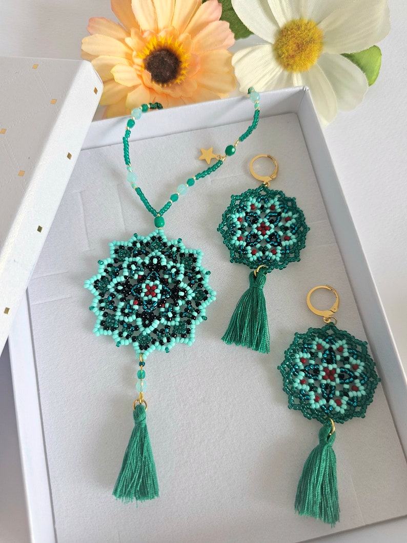 May include: A set of green and blue beaded jewellery with tassel accents. The necklace and earrings feature a mandala design with red accents. The jewellery is displayed in a white box.