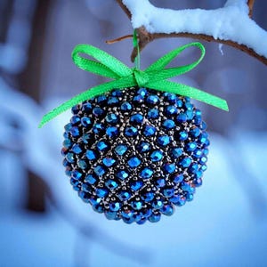 May include: A spherical ornament covered in iridescent blue beads, suspended from a snow-covered branch. A bright green ribbon is tied at the top. The ornament is approximately 3 inches in diameter, perfect for holiday decor.