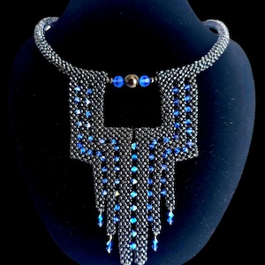 May include: A black and blue beaded necklace with a geometric design. The necklace features a square-shaped pendant with a cascading fringe of blue beads.