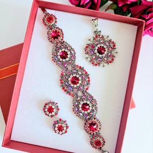Op de afbeelding: Een rode en zilveren kralen sieradenset in een rode doos. De set bevat een armband, een hanger en een paar oorbellen. De sieraden zijn gemaakt van kleine, ronde kralen en hebben een bloemmotief.