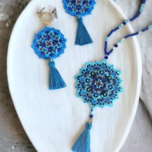 May include: A blue and black beaded necklace with a mandala pendant and tassel. The necklace is paired with matching earrings with blue and black beaded mandala pendants and tassels.