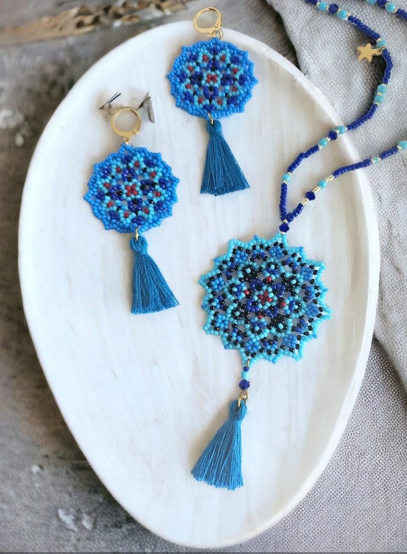 May include: A blue and black beaded necklace with a mandala pendant and tassel. The necklace is paired with matching earrings with blue and black beaded mandala pendants and tassels.