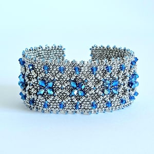 Peut inclure: Bracelet manchette en perles argentées avec des accents de cristaux bleus. Le bracelet mesure environ 3,8 cm de large. Le motif présente des fleurs en cristal bleu.