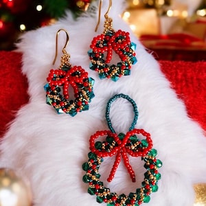 Op de afbeelding: Een set van drie kerstkrans oorbellen van kralen. De oorbellen zijn gemaakt van rode en groene kralen en hebben een gouden strik. De oorbellen worden getoond op een wit, pluche oppervlak.