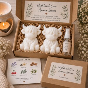 May include: A cardboard gift box containing two white Highland cow-shaped aroma stones made of natural plaster and a small clear spray bottle labelled A little scent goes a long way. Includes a scent ideas card and a branded box lid.