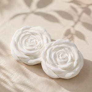 May include: Two white, matte-finish rose sculptures crafted with layered, overlapping petals. These circular floral objects feature a smooth, solid surface texture and are arranged side-by-side, showcasing intricate, realistic petal formations.