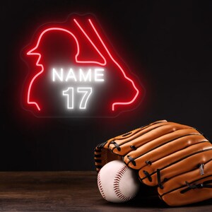 Puede incluir: Un letrero de ne&oacute;n rojo de un jugador de b&eacute;isbol con el nombre "NAME" y el n&uacute;mero "17" en blanco. Un guante de b&eacute;isbol marr&oacute;n y una pelota de b&eacute;isbol blanca est&aacute;n en primer plano.