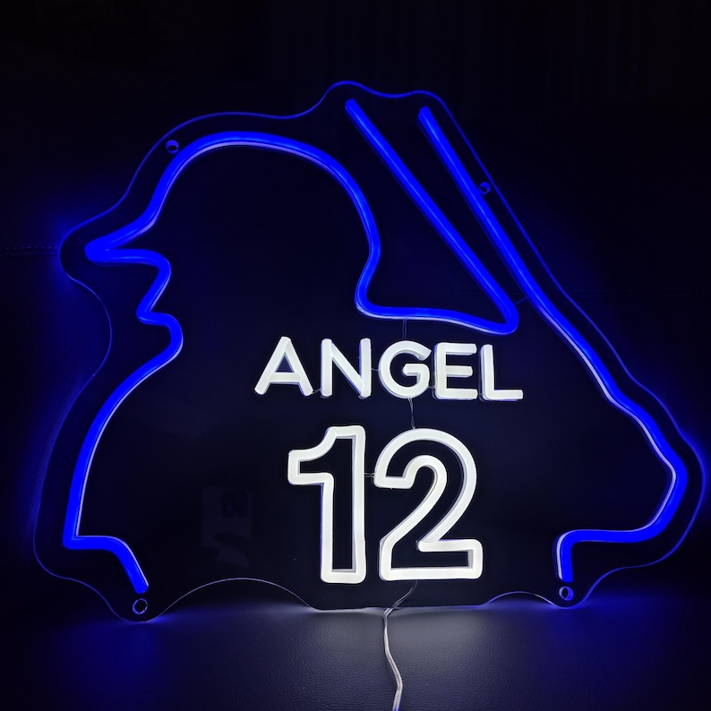 Puede incluir: Un letrero de ne&oacute;n azul con forma de circuito de carreras con el nombre "ANGEL" y el n&uacute;mero "12" en ne&oacute;n blanco.