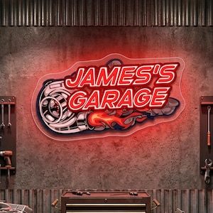以下が含まれることがあります： ターボチャージャーのグラフィックが付いた、赤と白の「JAMES'S GARAGE」ネオンサイン。サインは、ツールとツールボックスを備えた、質感のある灰色の壁に取り付けられています。サインは赤いネオンの輝きを持っています。