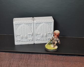Könnte beinhalten: Eine graue, 3D-gedruckte Miniatur-Burgmauer mit gewölbten Türen und dekorativen Details. Eine Miniatur-Eichhörnchen-Kriegerfigur steht in der Nähe auf einer grasbewachsenen Basis und hält ein Schwert. Die Szene spielt vor einem dunklen Hintergrund.