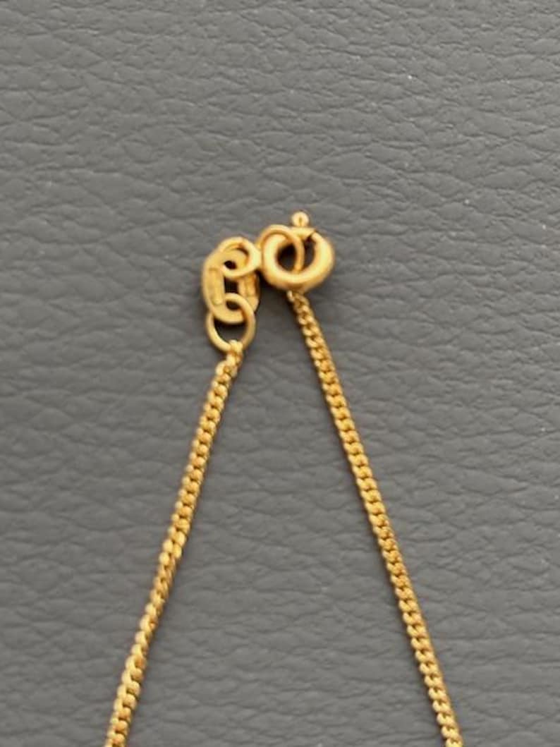 May include: Close-up of a gold-colored necklace chain with a lobster clasp. The chain is made of small, interconnected links, and the clasp is a simple, secure design. The necklace is displayed against a gray background.